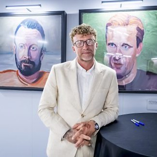 Zachariah Collett standing in front of two portrait paintings at the exhibition