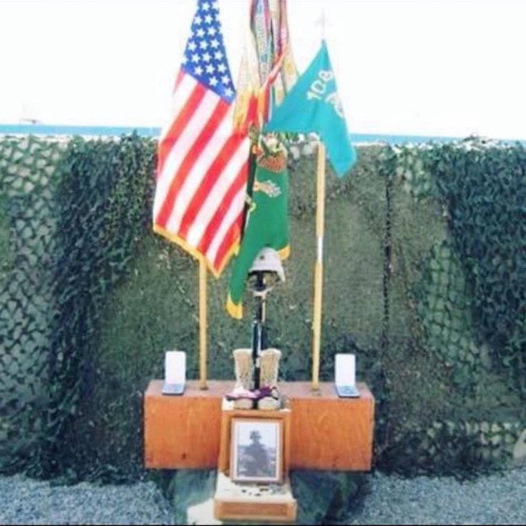 A memorial of boots, rifle and helmet set beneath unit and national colors
